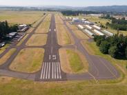 Aerial of airport runway, hangar buildings, trees, parked airplanes, sky