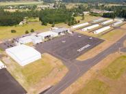 Aerial of airport runway, large hangar buildings, parked airplanes, trees in background