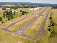 Aerial of airport runway with trees, sky and buildings in background