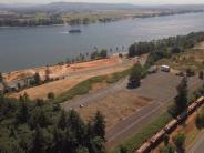 Aerial photo of river with ship going upriver, train hauling logs, land and trees