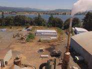 Buildings, steam, packaged product stacked up, river and trees in background