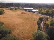 Open field with railroad track and road, buildings in the background and trees