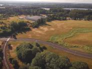 Open field with railroad track and road, river in the background and trees