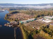 Aerial of river, dock, log yard and industrial buildings, trees and sky