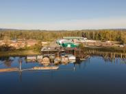 River, dock with boathouses, industrial building, log yard, trees in background