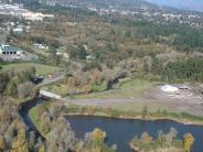 Aerial photo of river and land with trees, a few buildings, and a small bridge over a creek