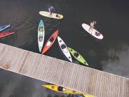 Kayaks tied up to the dock, two people paddle boarding in the river