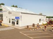 Exterior of the Scappoose Bay Paddling Center building, people walking with paddles, parked cars