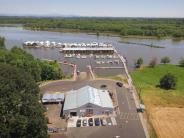 Building with parked cars outside, boat ramp, docks, moored boats, river, trees, sky