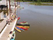 Dock with kayaks and paddle boards tied up, people kayaking in the distance, people on the dock in life jackets