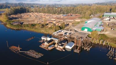 Aerial of river, dock with houseboats, log yard, and industrial building