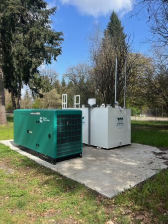 Green and white generators on a concrete pad with grass and trees in background